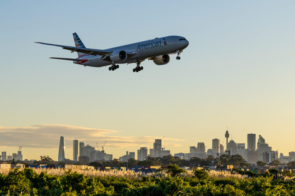 An American Airlines Boeing B777-323(ER) plane, registration N719AN, coming into land at Sydney Kingsford Smith Airport as flight AA73 from Los Angeles. In the background are skyscrapers in the central business district of Sydney. This image was taken from New Link Road, Mascot on a sunny, cold and windy morning shortly after sunrise on 9 May 2026.