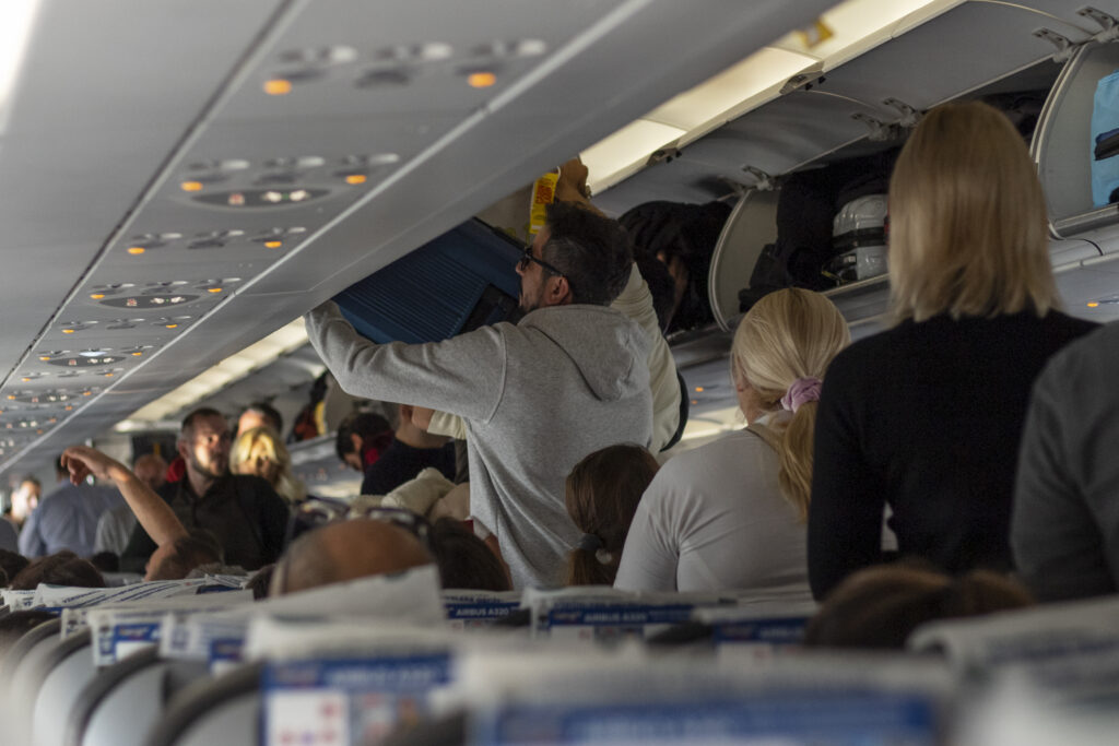Boarding a plane. Passengers stack baggage on luggage racks.