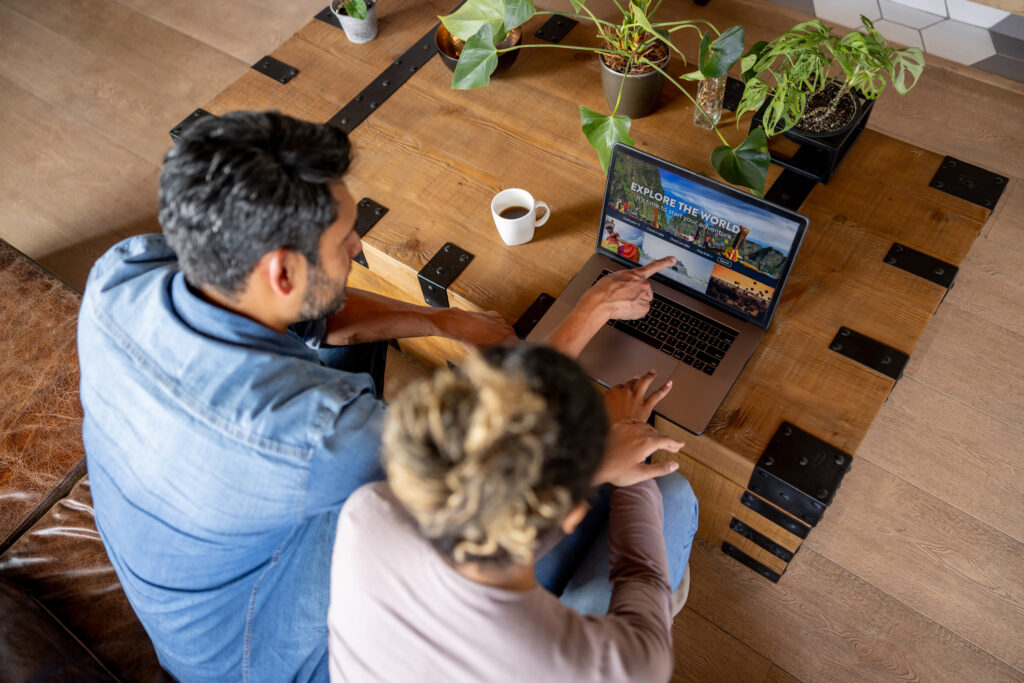 Happy couple at home booking a trip online using their laptop computer.