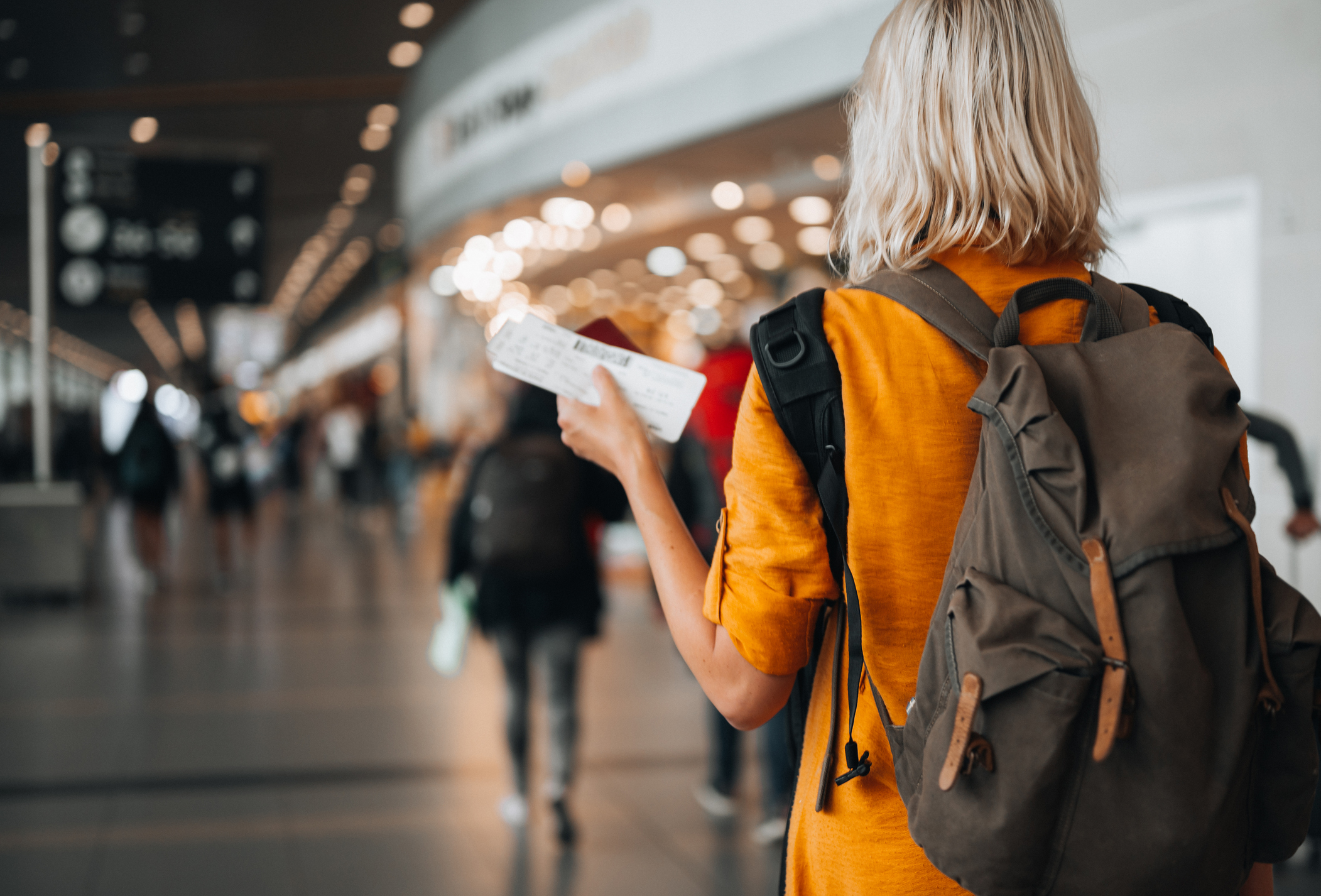 Rear view of a woman at the airport holding a passport with a boarding pass as she walks to her departure gate.