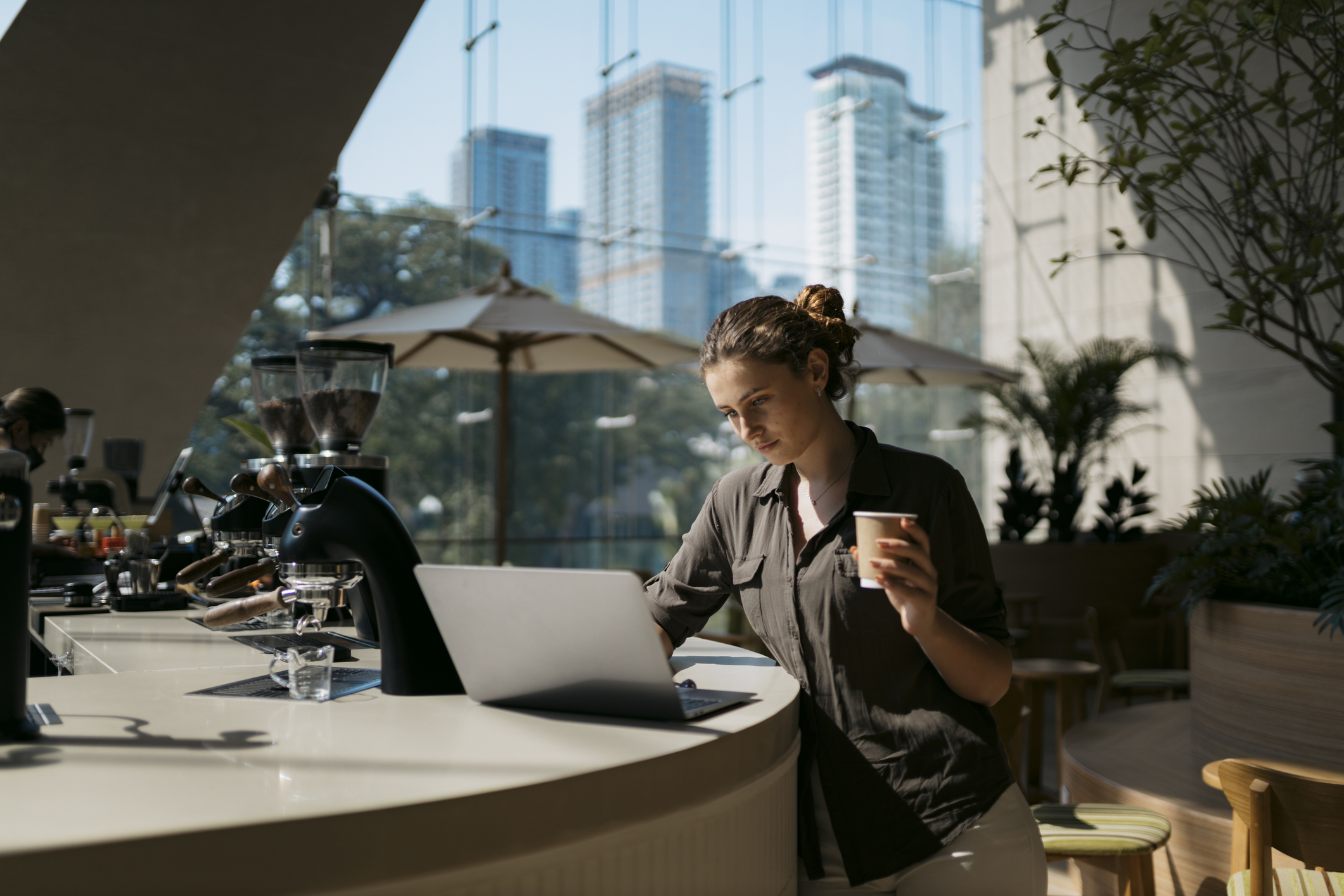 Confident young woman looking a laptop and drinking a coffee in a cafe. Female customer drinking coffee and browsing net on laptop at internet cafe.