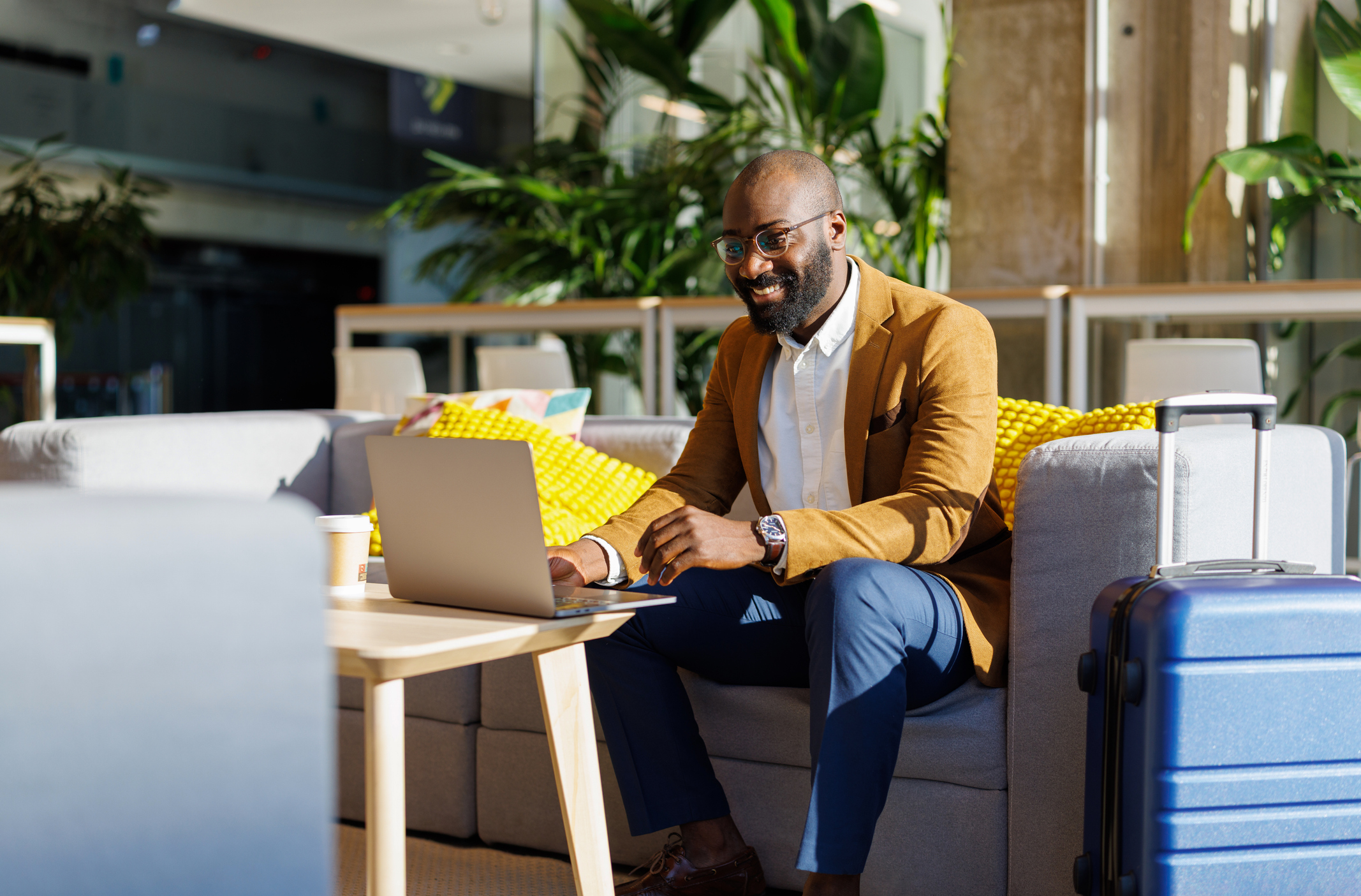 Adult man sitting with luggage, smiling while using laptop