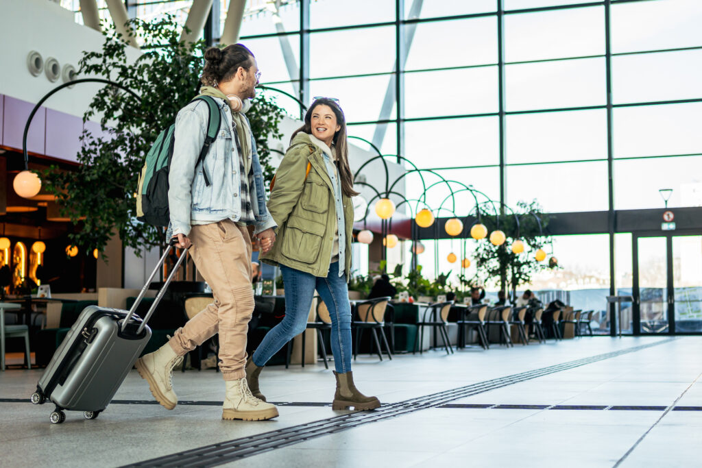 Young couple walking in the train station, pulling suitcase and wearing backpacks, ready for vacation