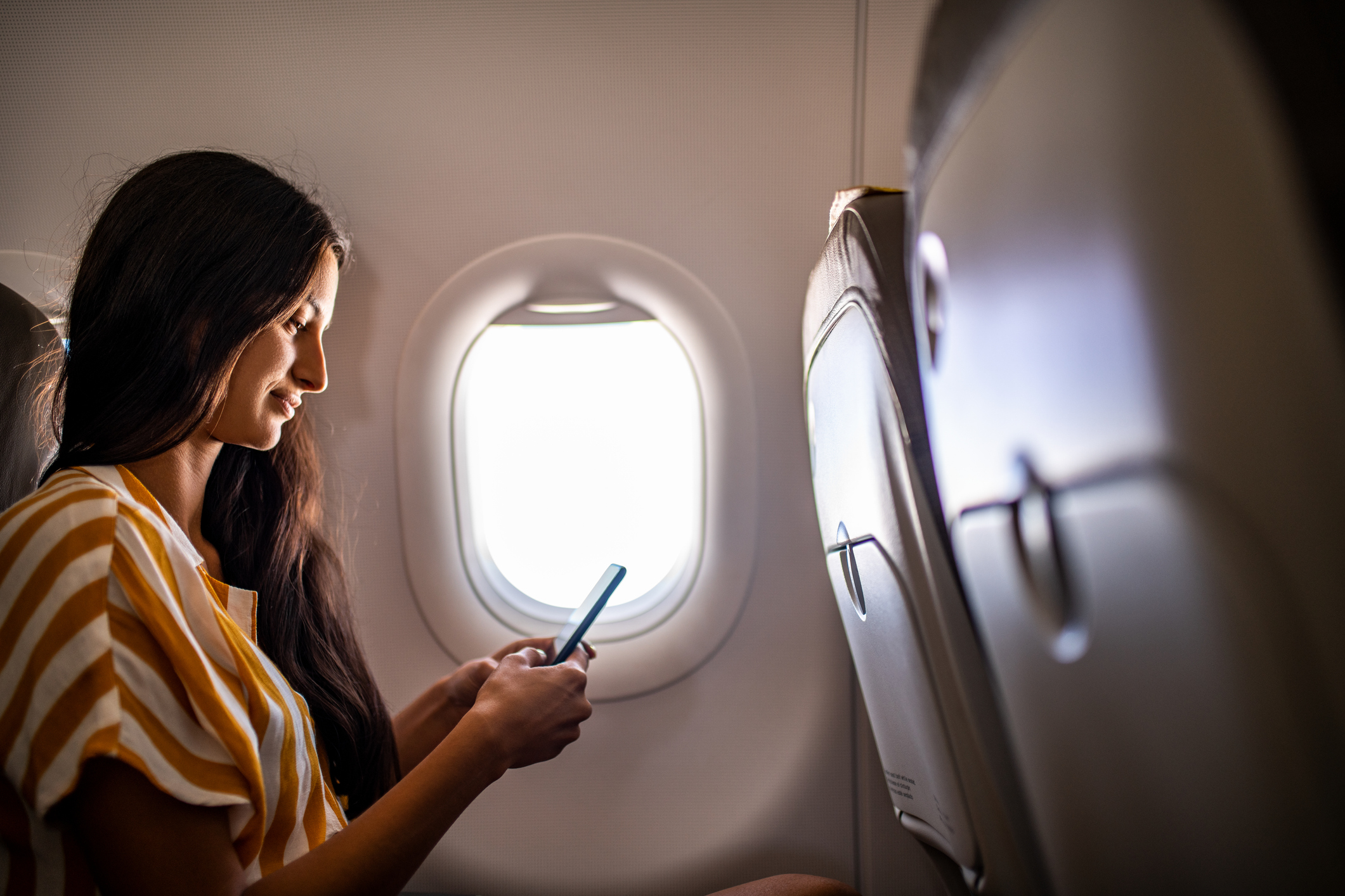 Young smiling woman using mobile phone in the airplane.