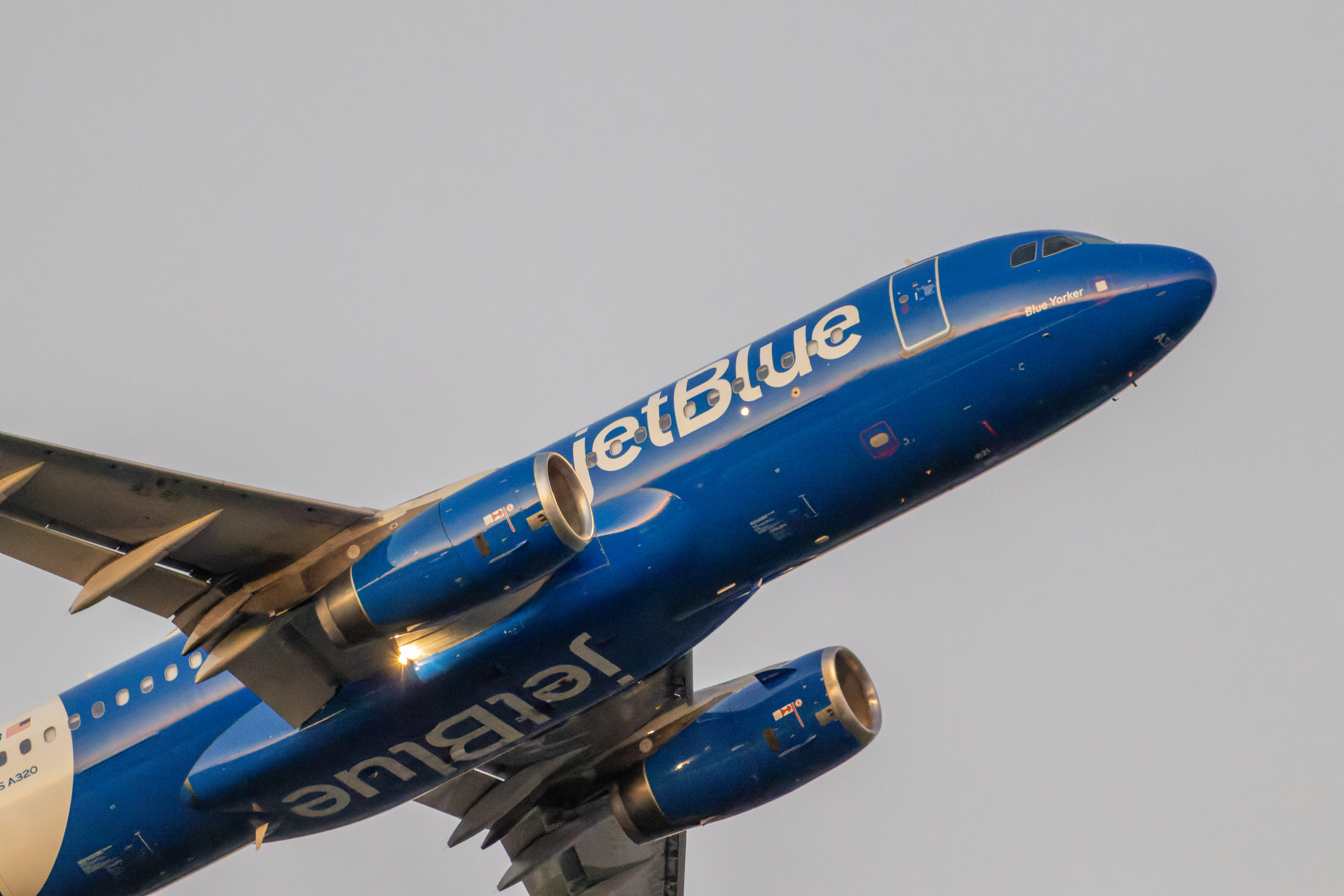 Close-up view of a JetBlue Airbus A320 aircraft in its “Blue Yorker” livery climbing after takeoff from Ronald Reagan Washington National Airport, captured in warm evening light.